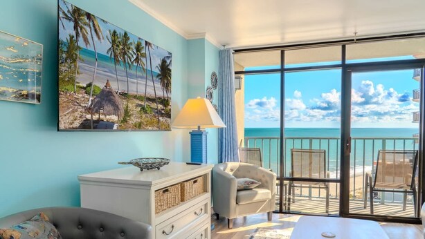 A room with a view of the ocean, a white dresser, a grey armchair, a white table, and a painting of a beach scene. - Sand Dunes 1246 (Myrtle Beach)
