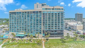 A multi-story hotel with a modern glass facade, a swimming pool, and a landscaped courtyard. - Sand Dunes 1246 (Myrtle Beach)