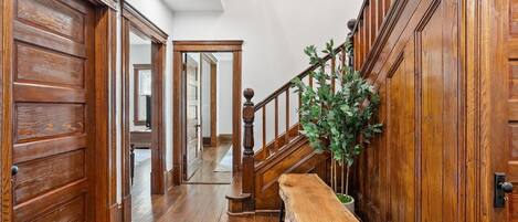 A wooden hallway with a bench, a staircase, and a potted plant.