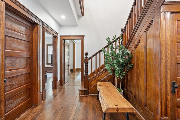 A wooden hallway with a bench, a staircase, and a potted plant.