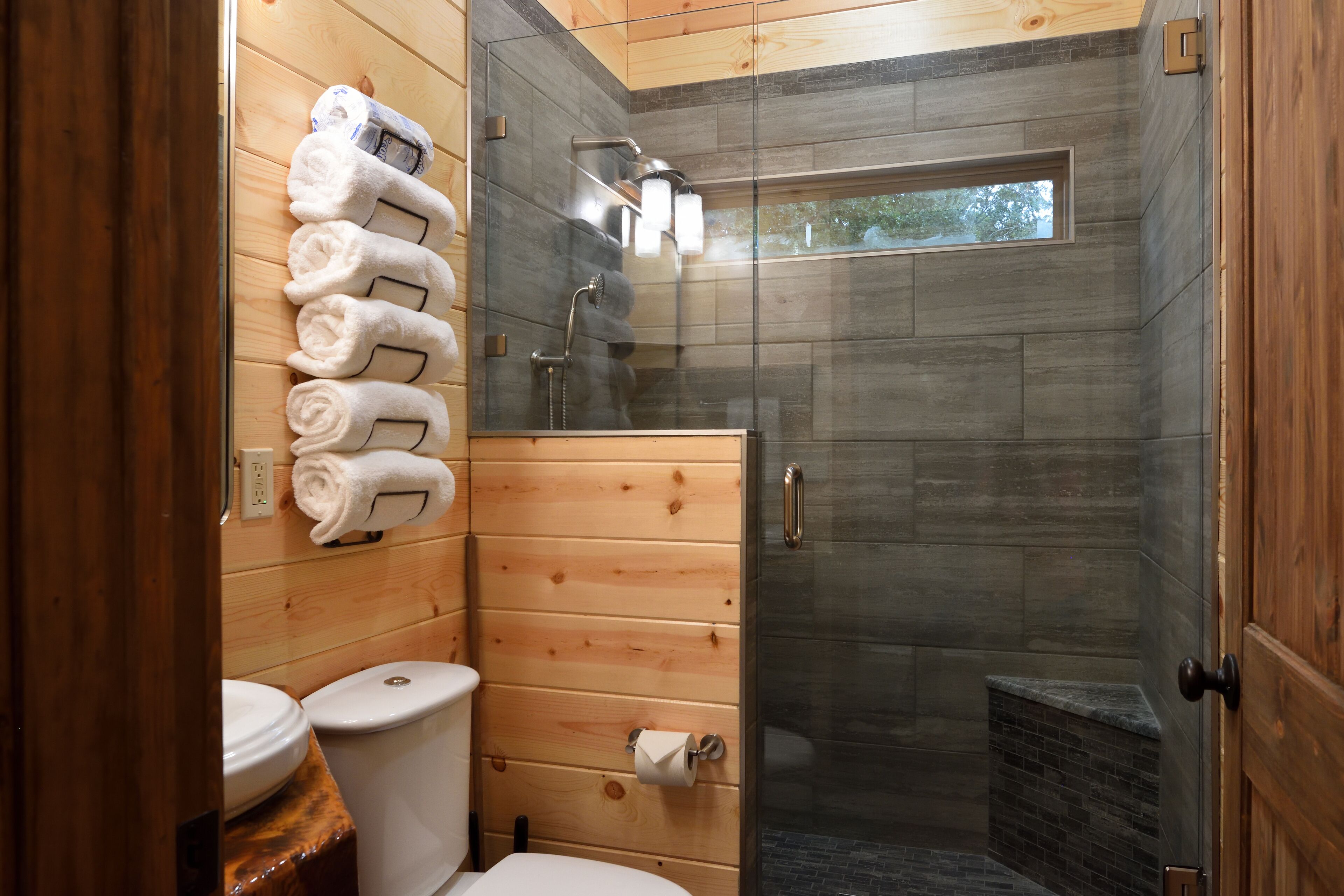A wooden-paneled bathroom with a glass-enclosed shower, a toilet, and a sink.