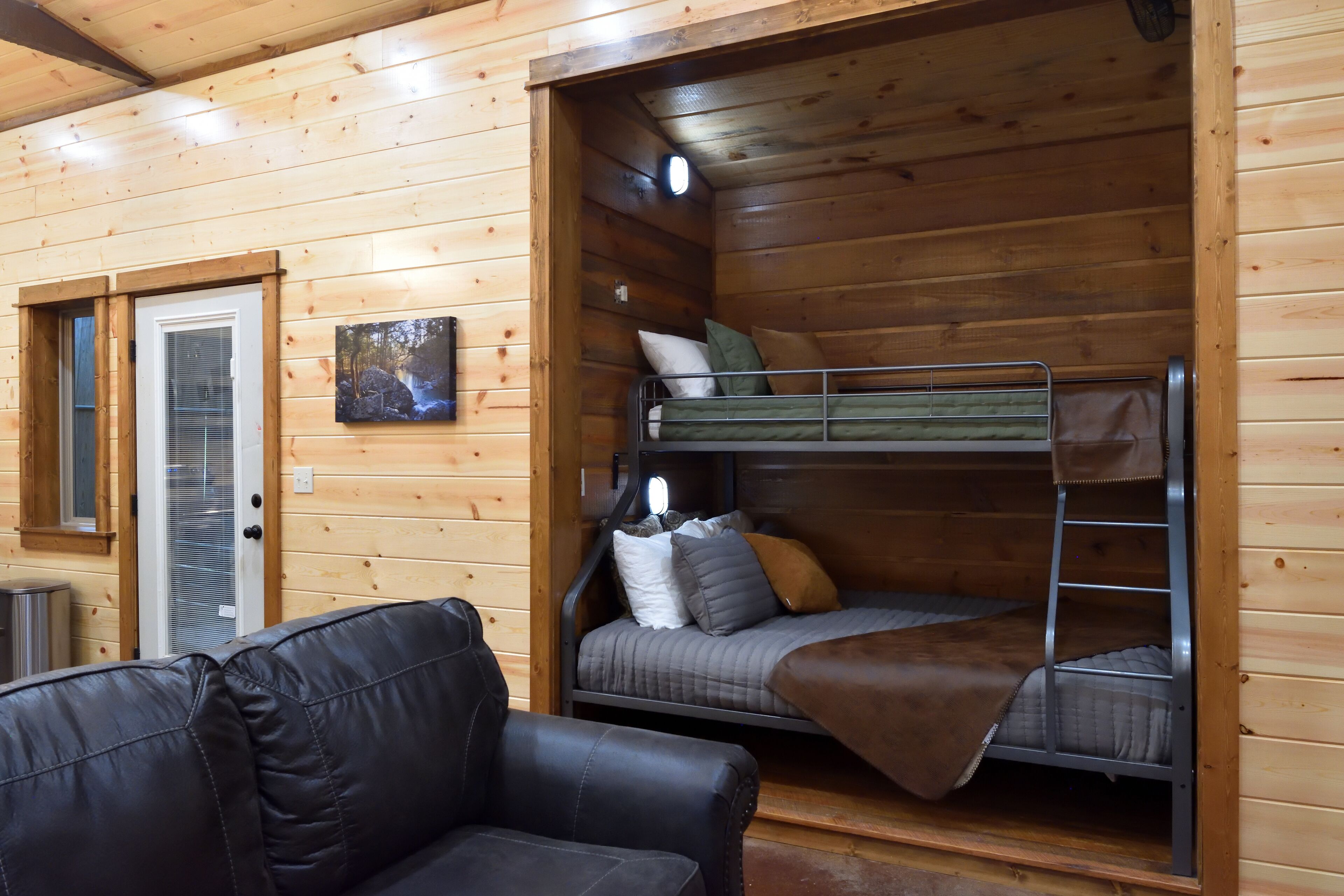 Interior de una cabaña con literas, un sofá y una ventana con persianas.