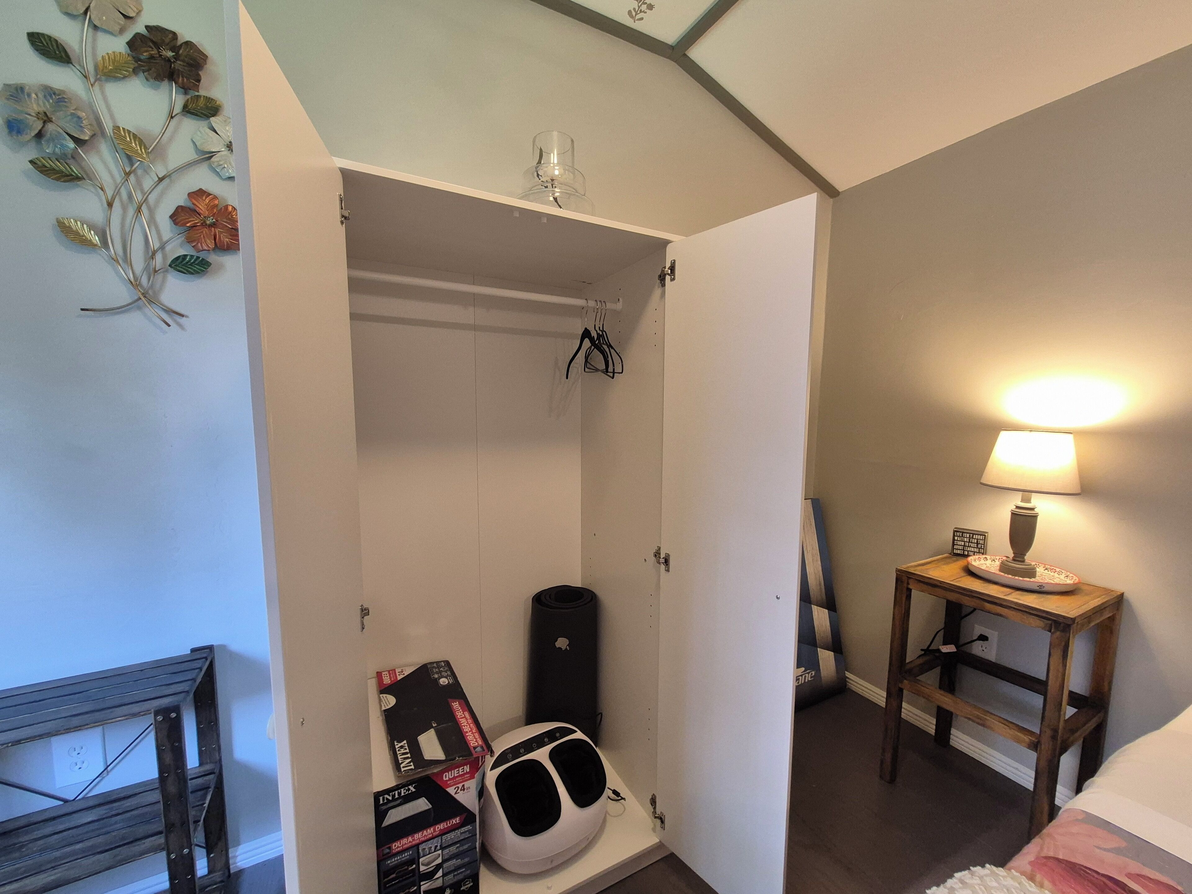 Quarto de hotel com guarda-roupa, mesa de cabeceira com abajur, uma guitarra e um arranjo floral de metal decorativo.