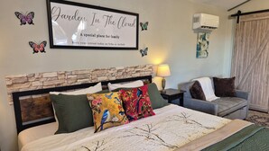 A hotel room with a bed, a chair, a nightstand, a lamp, and a framed sign on the wall. - Garden Retreat in St. Cloud with WiFi, AC. (St. Cloud)