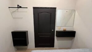Une chambre à coucher avec un lit, une porte, une petite étagère et un miroir.