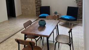 Un coin repas avec une table et des chaises en bois, un coussin bleu sur une chaise et une fenêtre donnant sur un paysage verdoyant.