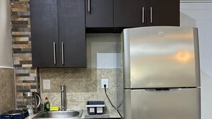 Une cuisine moderne avec des meubles de couleur sombre, un réfrigérateur en acier inoxydable, un plan de travail en granit et un pare-feu en carreaux.