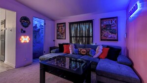 Un salon avec un canapé, une table basse en verre et un néon fixé au mur.