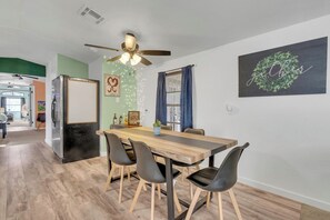 A dining area with a wooden table, four chairs, a ceiling fan, and a wall with a wreath and a sign.