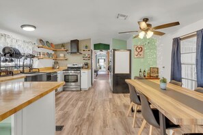 A modern kitchen with a central island, a dining area with a long table, and a ceiling fan.