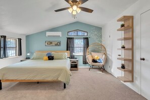 Ein Schlafzimmer mit einem Bett, einem Deckenventilator, einem Fenster, einem Sessel und einem Regal.