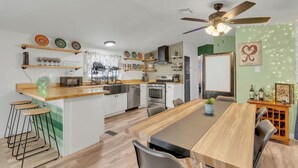Une cuisine moderne dotée d’un îlot central, de tabourets de bar, d’une table à manger et d’un ventilateur de plafond.