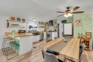 A modern kitchen with a central island, bar stools, a dining table, and a ceiling fan.