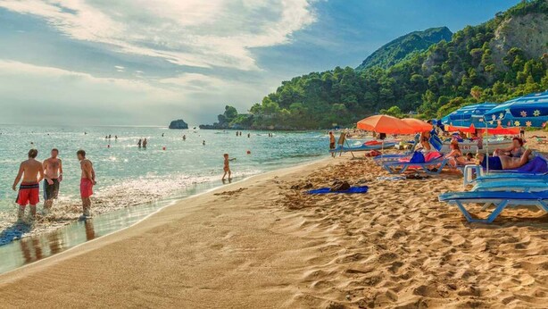 Une plage où l’on peut se baigner et bronzer, avec des parasols et un paysage montagneux en arrière-plan.