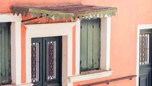 Un bâtiment doté d’une façade orange remarquable, de volets verts et d’un porche carrelé.