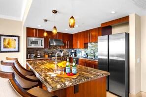 Una cocina moderna con una isla de mármol, electrodomésticos de acero inoxidable, armarios de madera e iluminación colgante.