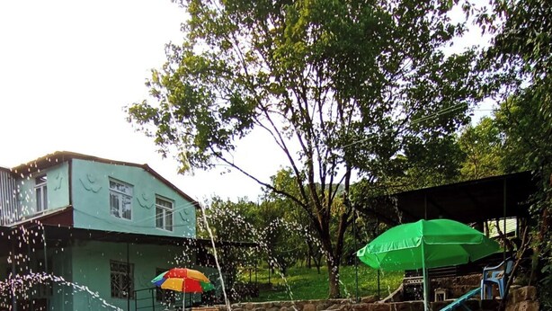 A swimming pool with water jets, a green building, and a covered area with a green umbrella. - Spacious 5-bedroom villa with swimming pool  WiFi and AC in lovely Alaverdi (Alaverdi)
