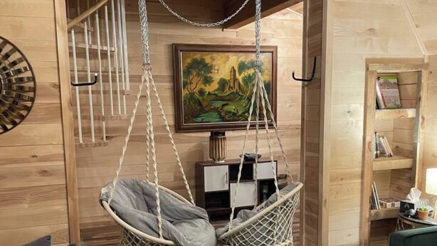 Ein gemütliches Zimmer mit Hängesessel, gestuftem Sofa, Holzregal und einem Bild an der Wand.