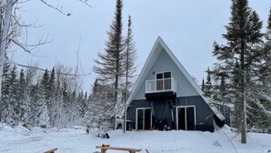 Eine dreieckige Hütte mit Balkon, umgeben von schneebedeckten Bäumen.