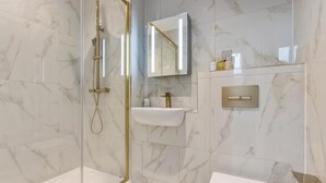 A modern bathroom with a glass-enclosed shower, a pedestal sink, and a wall-mounted mirror. - Flat 1 Saarb Apartments  (Leatherhead)
