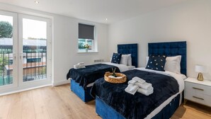 A modern bedroom with two beds, a balcony, and a window with a view. - Flat 1 Saarb Apartments  (Leatherhead)