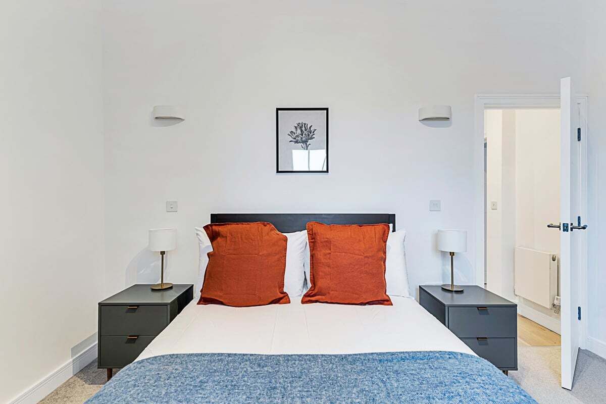 A modern bedroom with a large bed, two nightstands, a framed picture on the wall, and a door to the right.