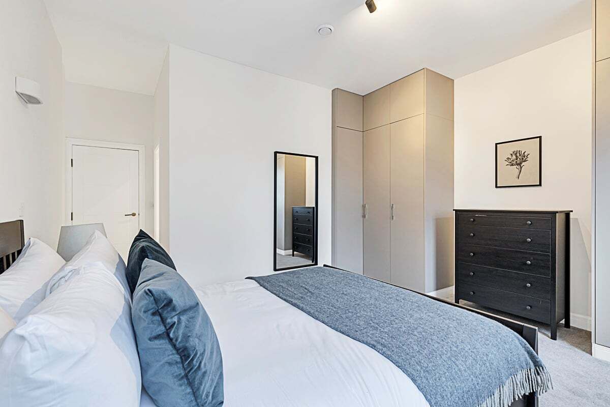A bedroom with a bed, a dresser, a wardrobe, and a mirror.