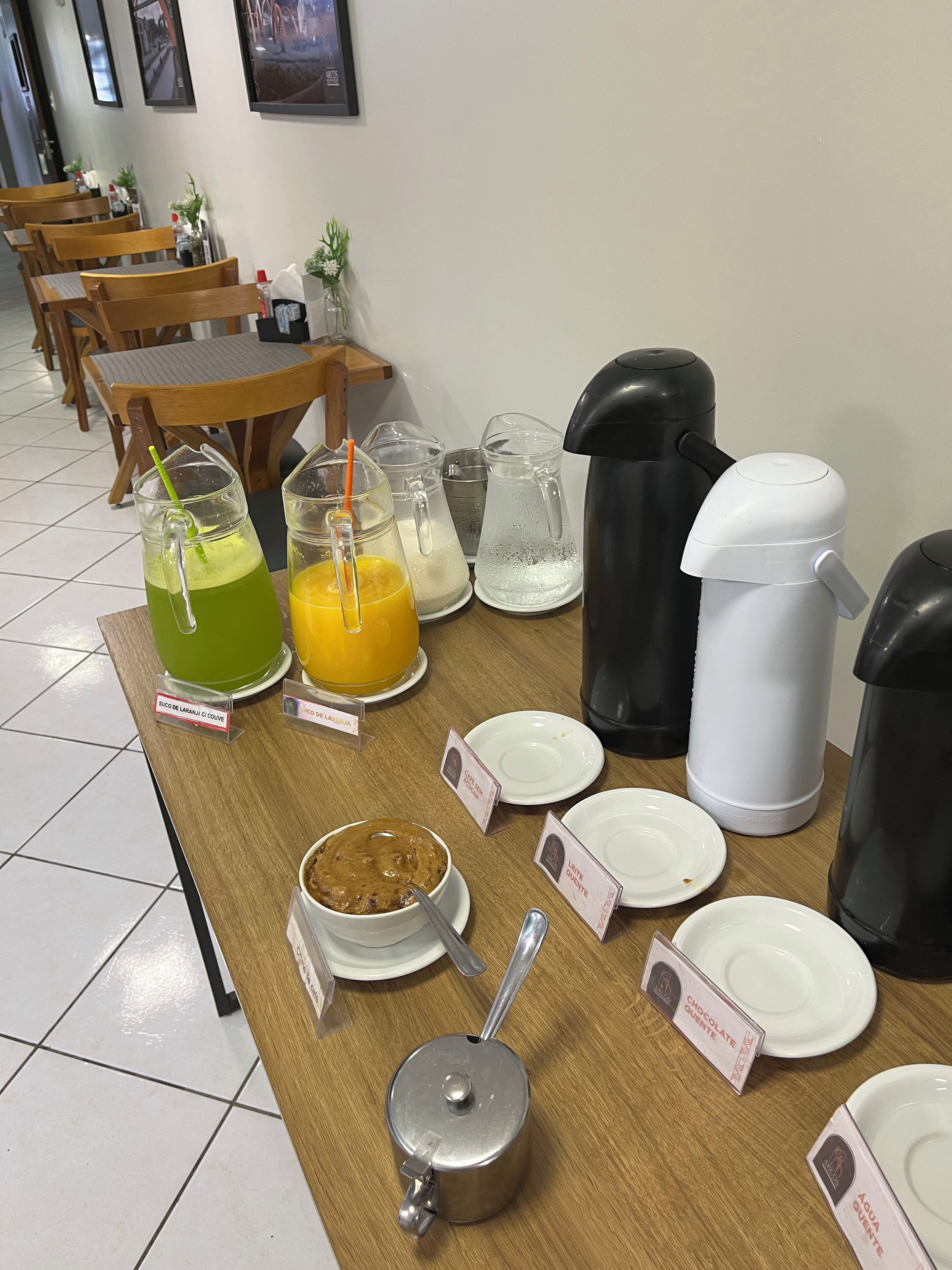 A breakfast buffet with various drinks, a coffee maker, and labeled dishes.