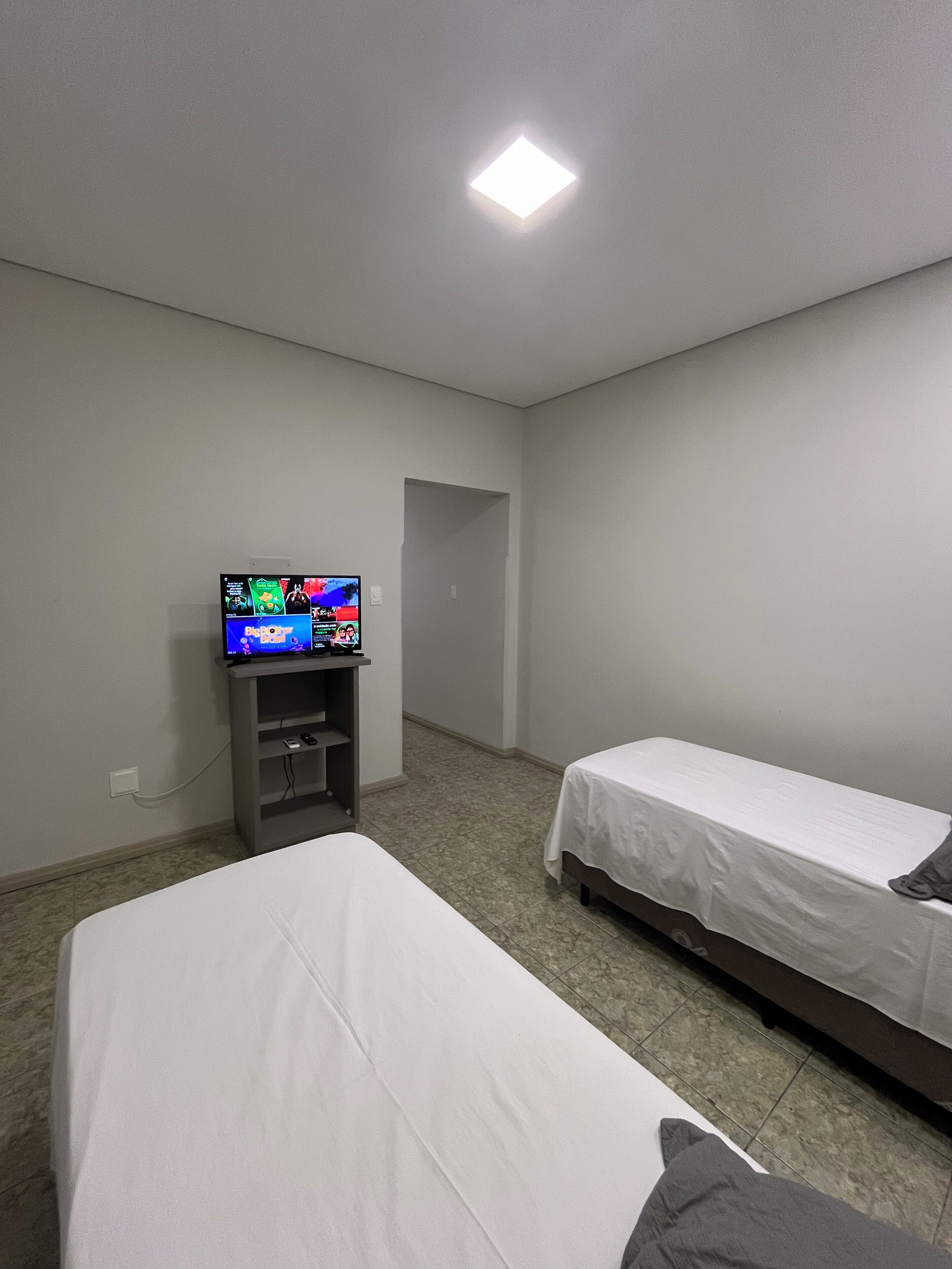 Una habitación con dos camas individuales, un televisor sobre un mueble bajo y una puerta que da a otra estancia.