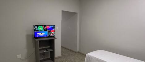 Una habitación con dos camas individuales, un televisor sobre un mueble bajo y una puerta que da a otra estancia.