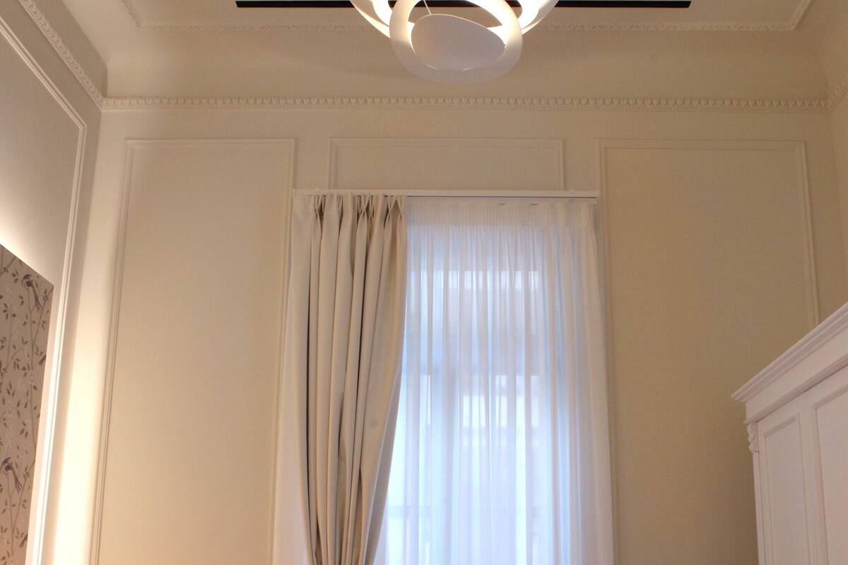 Quarto com uma cama grande, um lustre, um guarda-roupa e uma janela com cortinas.