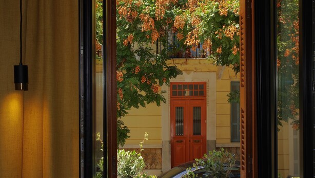 Une vue à travers une fenêtre, avec une porte en bois et un bâtiment jaune en arrière-plan.