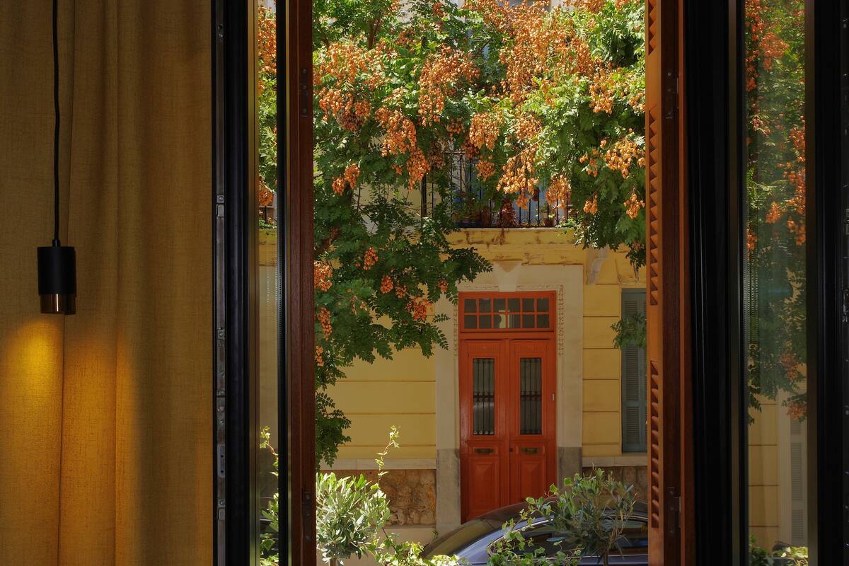 Vista pela janela, com uma porta de madeira e um edifício amarelo ao fundo.