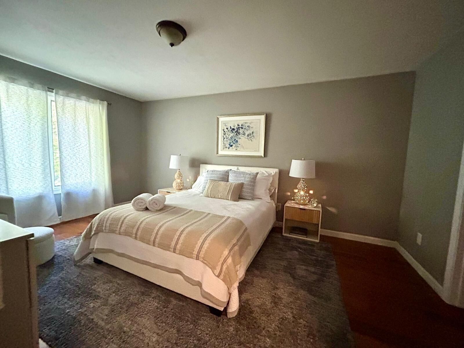 A bedroom with a large bed, two bedside tables with lamps, a window with curtains, and a ceiling light.