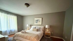 Een slaapkamer met een groot bed, twee nachtkastjes met lampen, een raam met gordijnen en een plafondlamp.