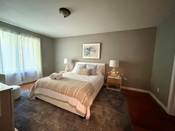 A bedroom with a large bed, two bedside tables with lamps, a window with curtains, and a ceiling light.
