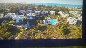 An aerial view of a residential area with multiple white buildings, a swimming pool, and a clear view of the ocean. - A charming two-bedroom beach front condo, Shell Island Beach Club, Sanibel. (Sanibel)