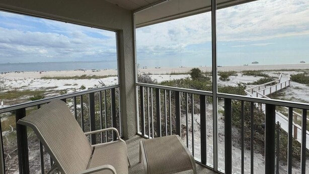 A balcony with two wicker chairs overlooking a beach with a boardwalk and dunes. - A charming two-bedroom beach front condo, Shell Island Beach Club, Sanibel. (Sanibel)