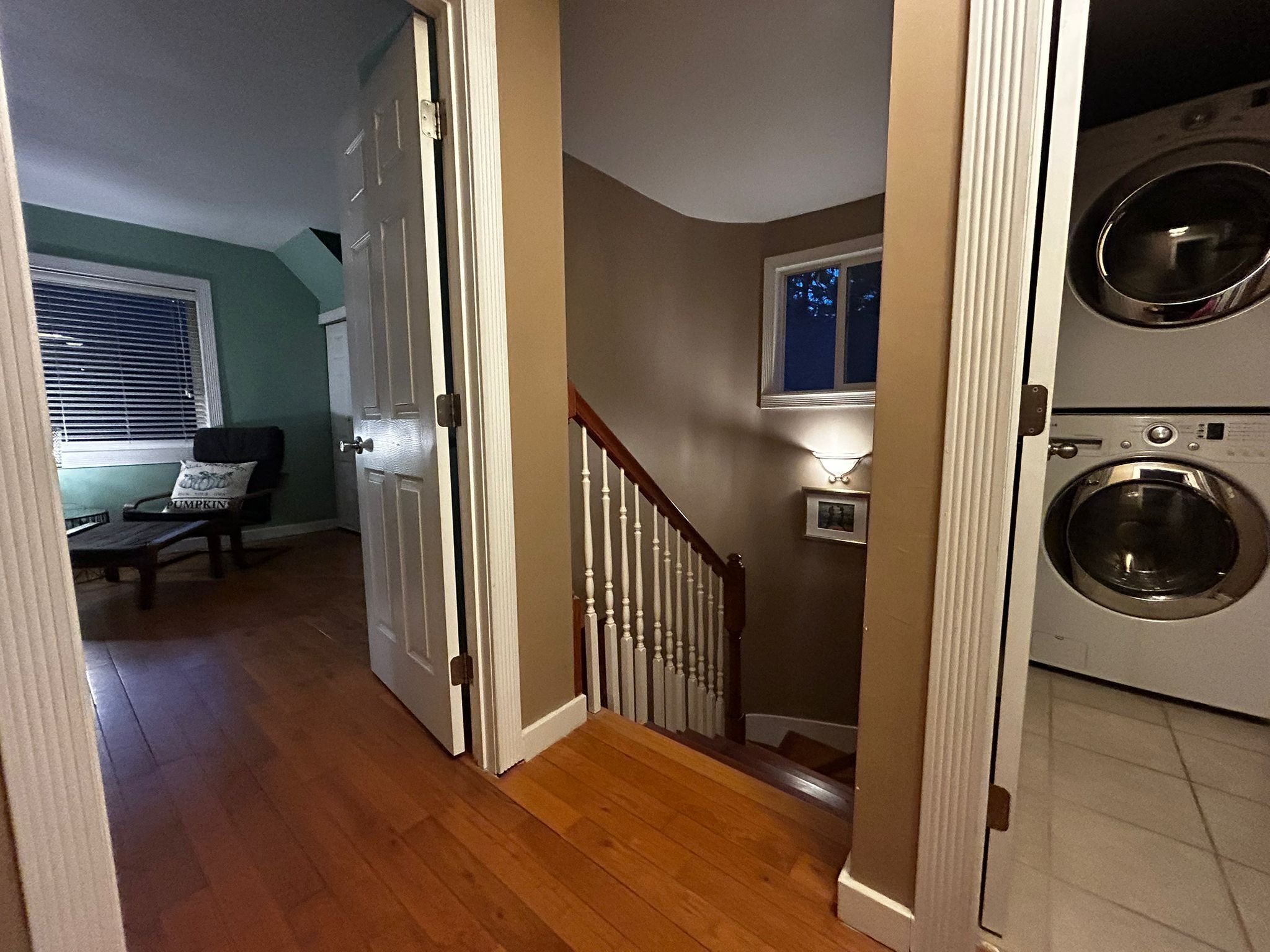 Un couloir avec un plancher en bois, un escalier, une porte, un banc avec un coussin et un espace buanderie équipé de deux machines à laver.