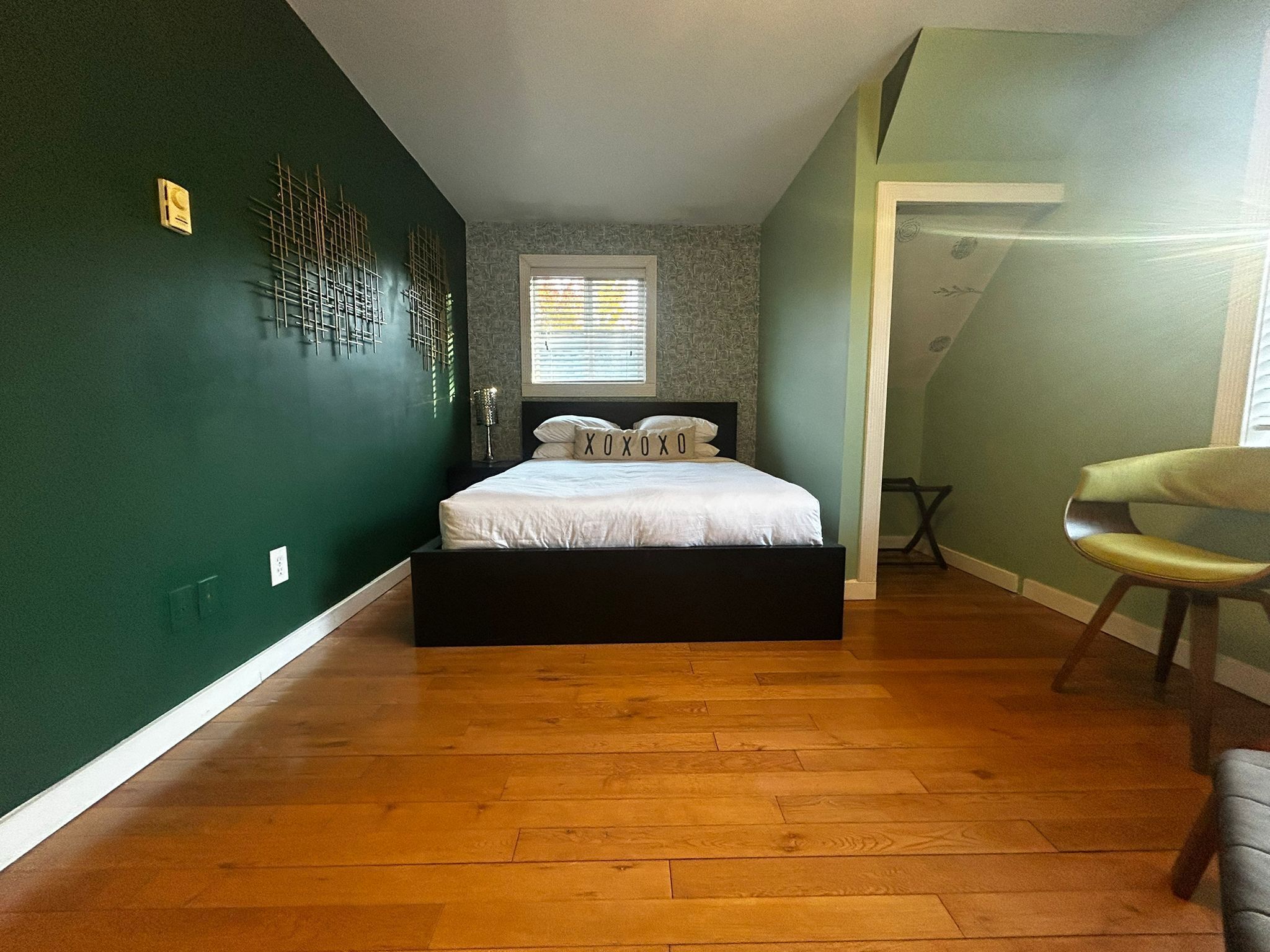 A bedroom with a bed, a chair, a window, and a wall with a decorative panel.