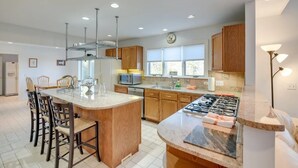 Una cocina moderna con una isla central, armarios de madera, electrodomésticos de acero inoxidable y un ventanal que proporciona luz natural.