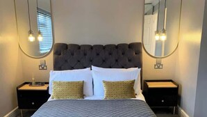 A bedroom with a large bed, two nightstands, a mirror, and pendant lights.