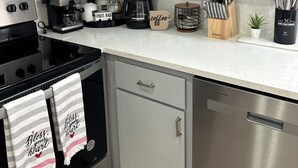 A modern kitchen with white cabinets, a black stove, a coffee maker, and various kitchen utensils.