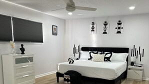 A modern bedroom with a bed, bedside tables, a ceiling fan, and a window with blinds.
