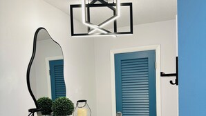 A hallway with a blue door, a white shelf with decorative items, a mirror, and a modern light fixture.