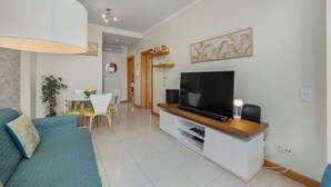 Uma sala de estar moderna com um sofá, uma TV e uma área de jantar com cadeiras e uma mesa.