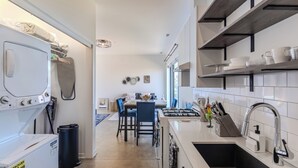 Eine moderne Küche mit weißen Schränken, einer Spüle aus Edelstahl und einem Essbereich mit blauen Stühlen und einem Tisch.