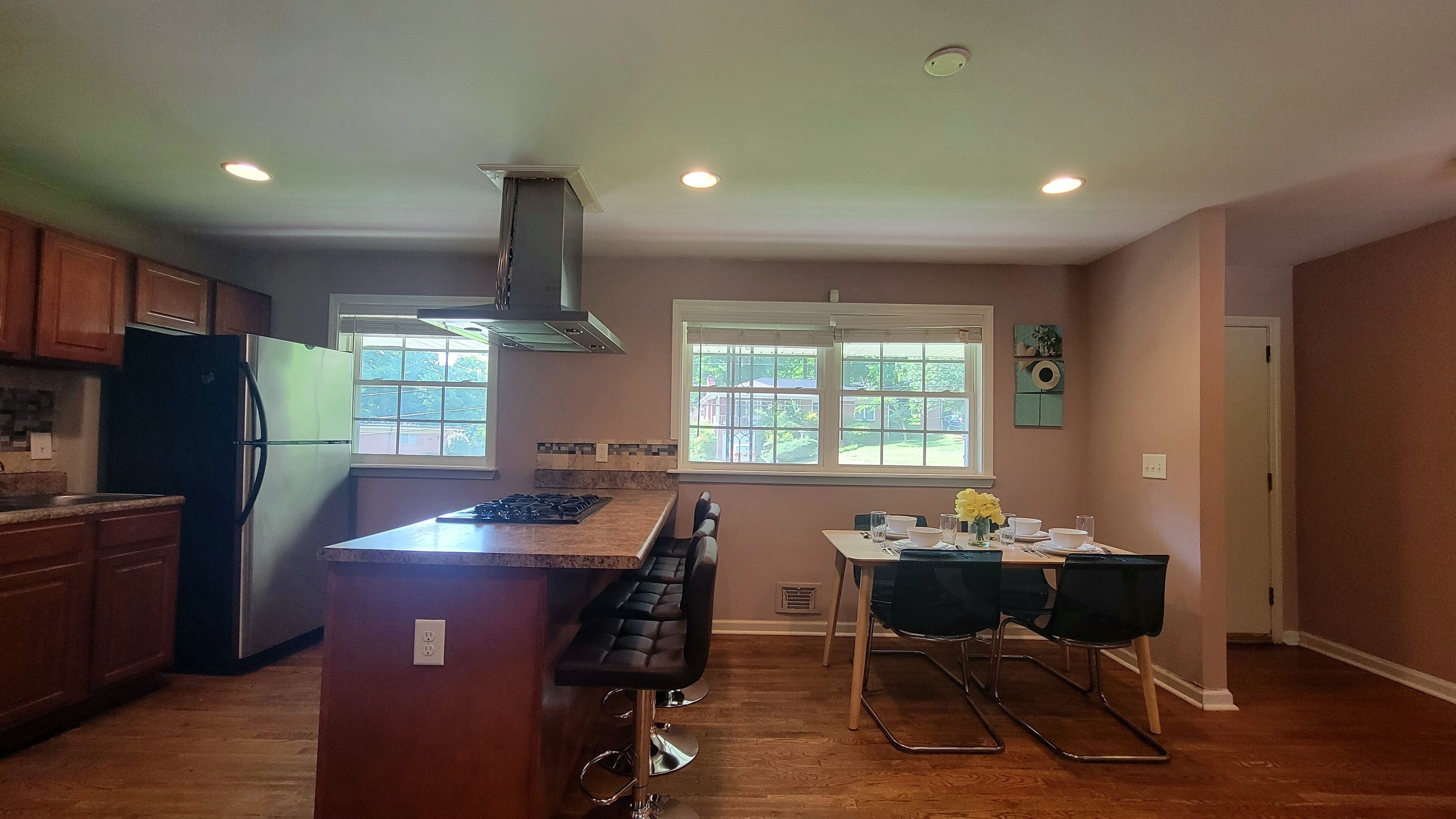 A kitchen with a central island, a dining area with a table and chairs, and a window with a view of greenery.