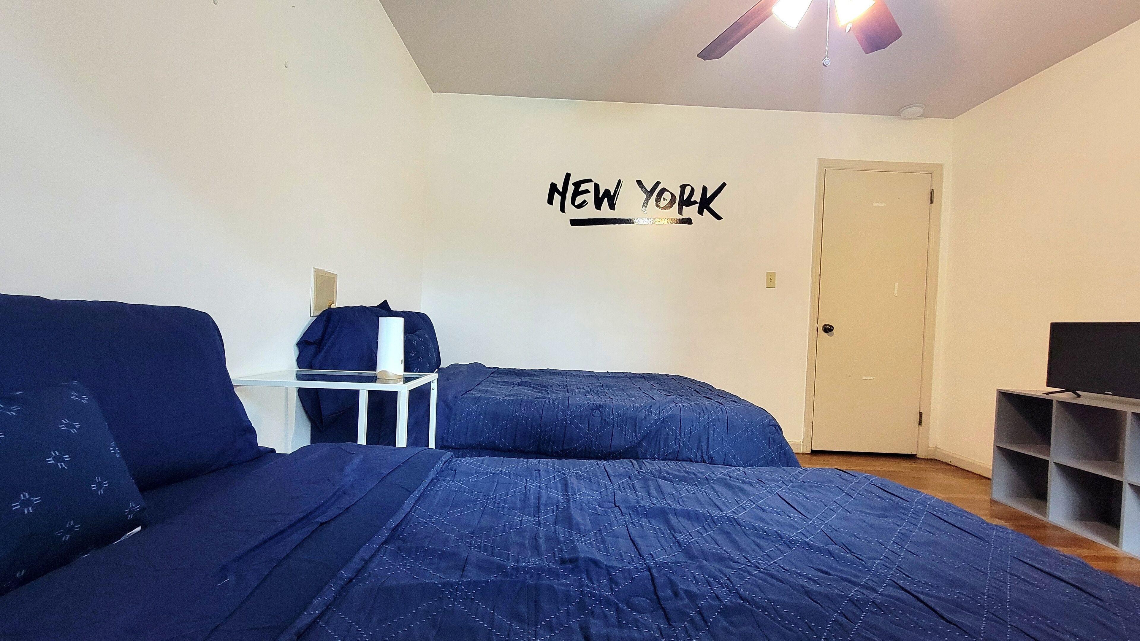 A bedroom with a bed, a desk, a chair, a TV, and a door.
