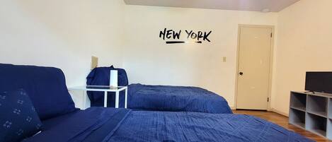 A bedroom with a bed, a desk, a chair, a TV, and a door.